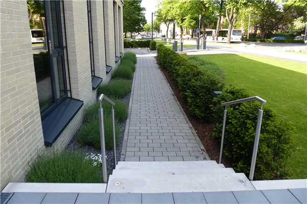 Gepflasterter Gehweg entlang eines Gebäudes mit Rasenfläche