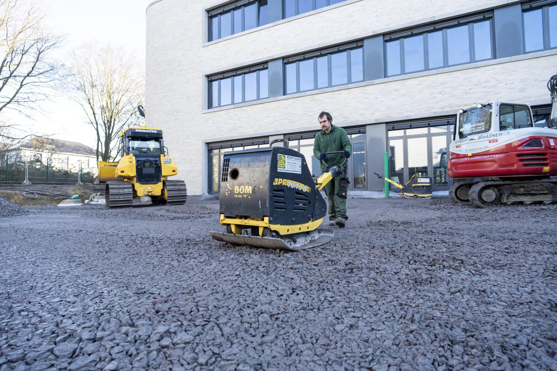 Mitarbeiter mit Rüttelplatte neben dem Radlader