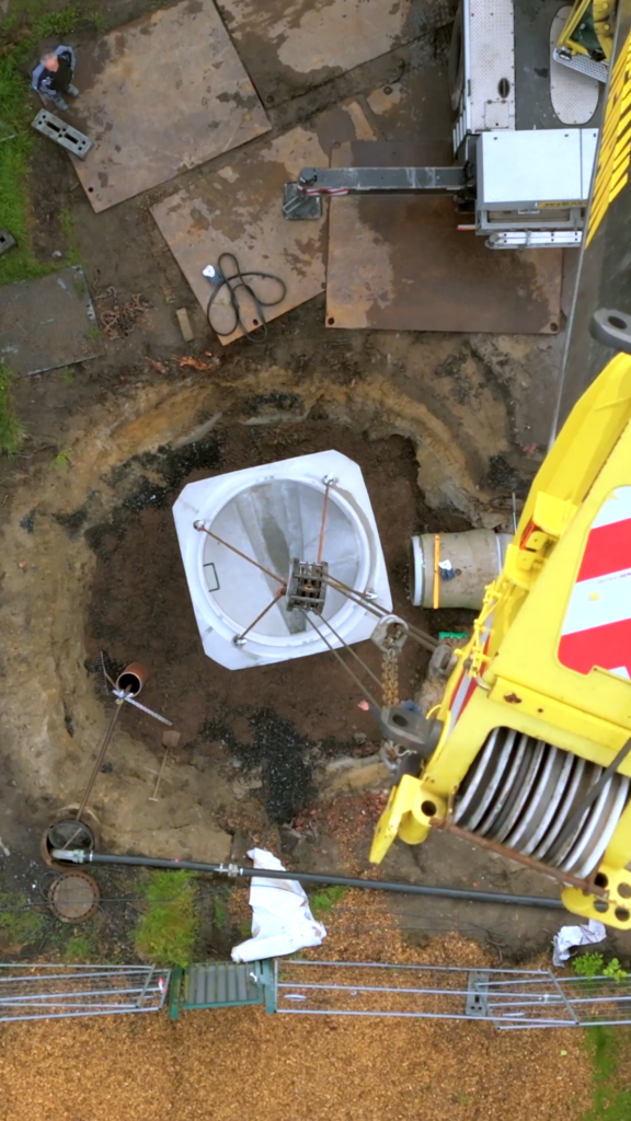 Betonschacht wird per Kran in eine Baugrube gesetzt