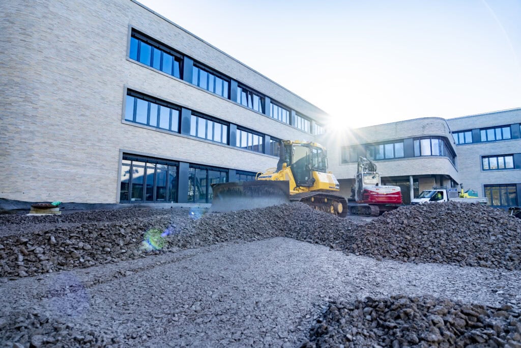 Schulgebäude mit blauer Fassade während der Außenanlagenarbeiten