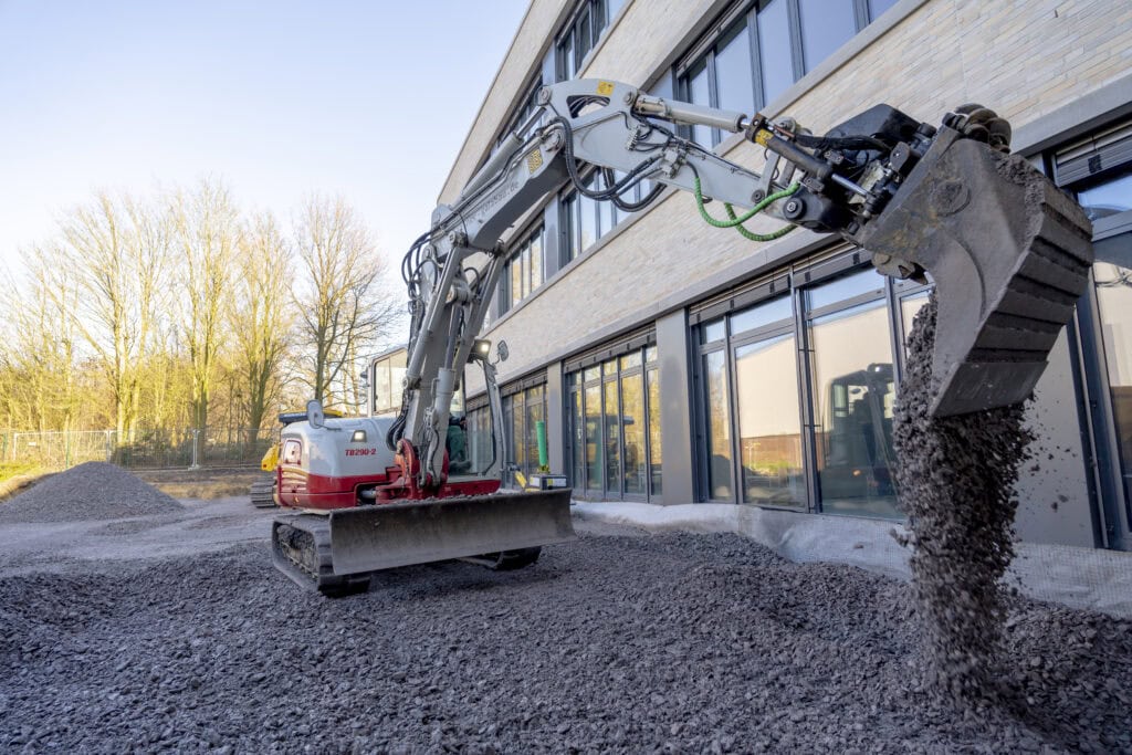 Bagger bei Erdarbeiten vor einer Glasfassade