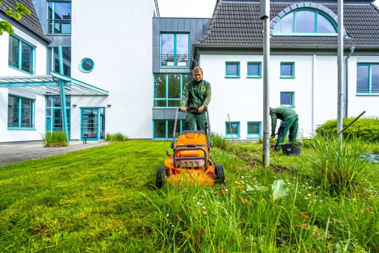 Mitarbeiter mäht den Rasen vor einem Wohngebäude